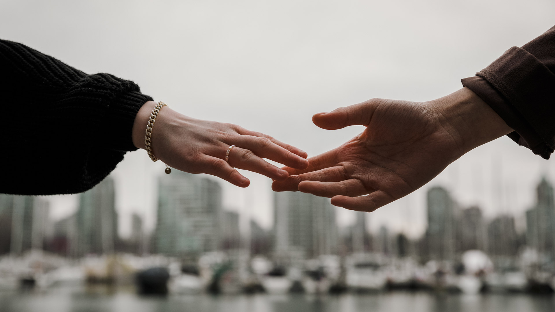 Two hands reaching together with a skyline in the background