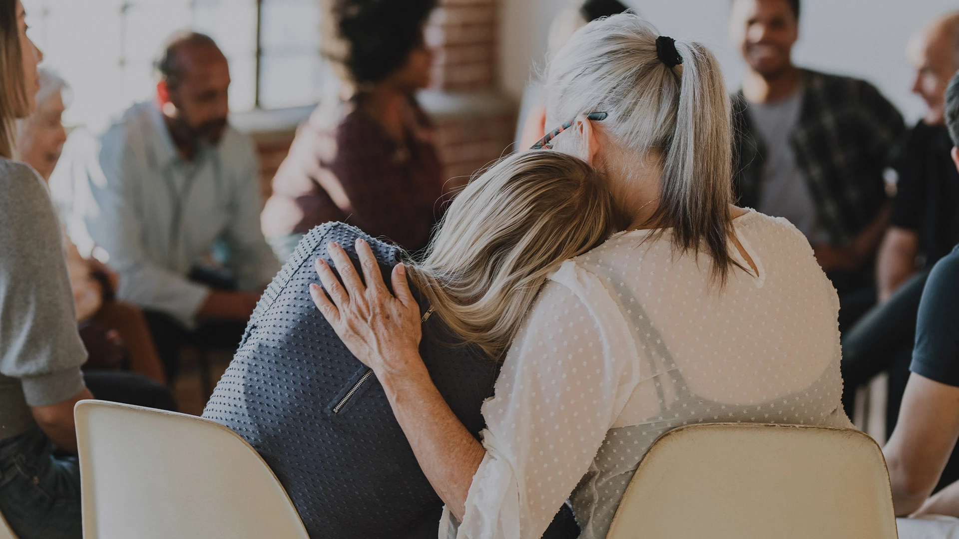 Two women sitting in a group embracing, recovery is a family journey
